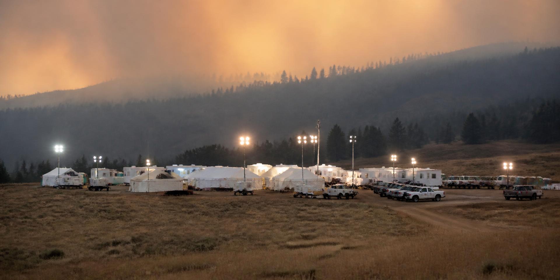 Wildland fire incident command post at dusk under a smoke-hazed ridgeline